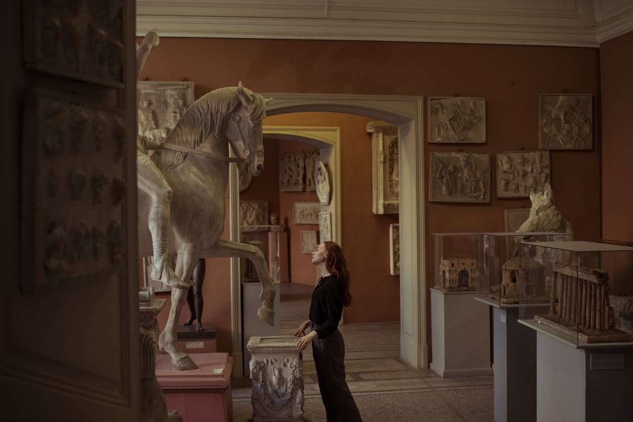 our-story Woman admiring a horse sculpture in an art museum, surrounded by classical artworks.