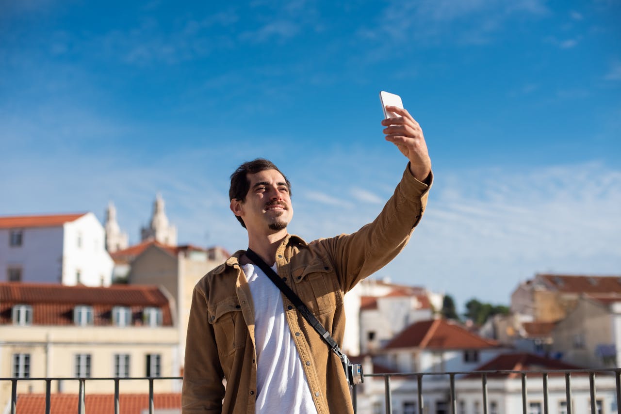 gallery-04 A man capturing a selfie against a picturesque sunlit cityscape with a clear blue sky.